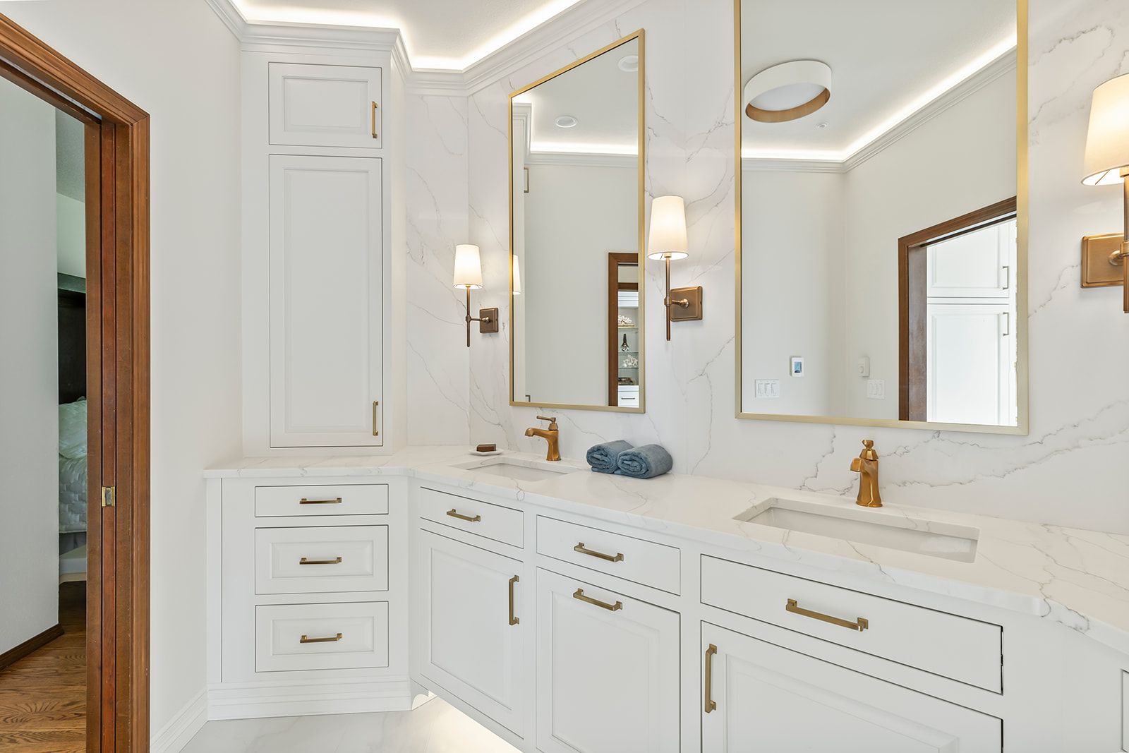 White primary bathroom with raised-panel vanity, brass fixtures and lighted mirrors