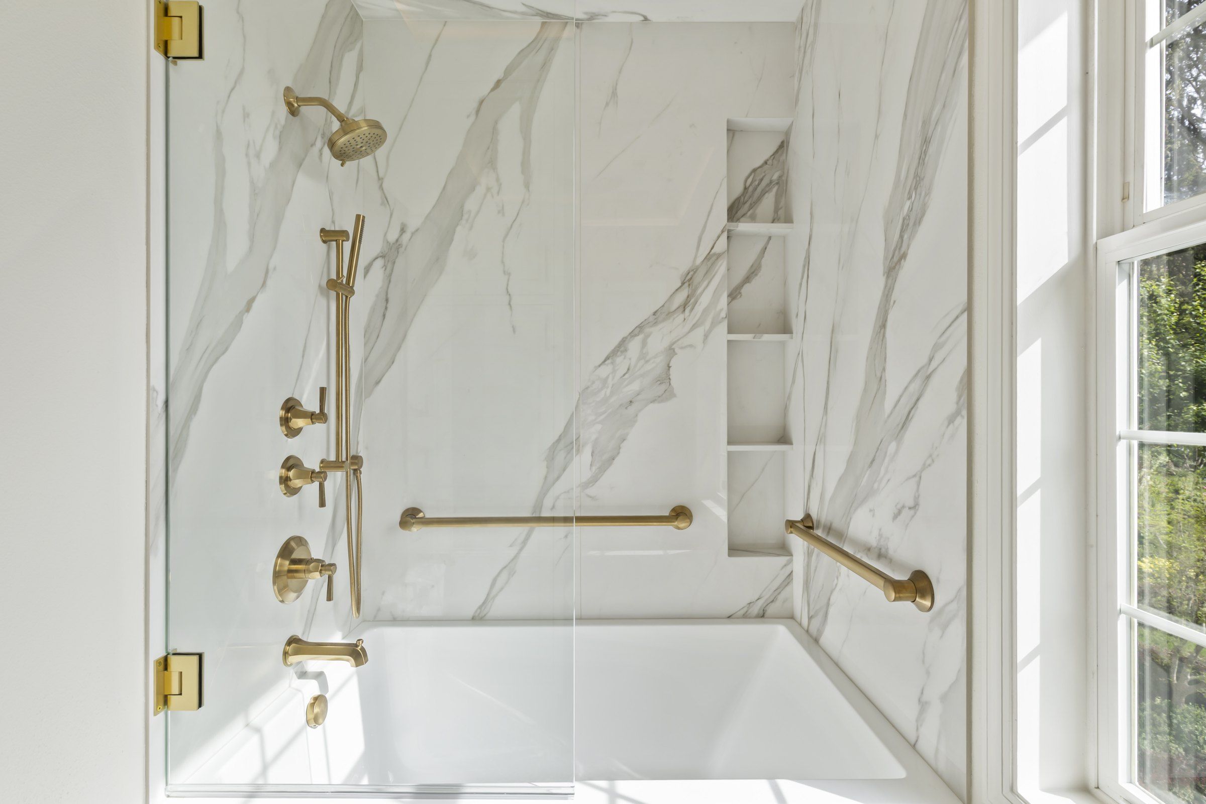 Brushed gold shower fixtures and grab bars on marble-look wall panels