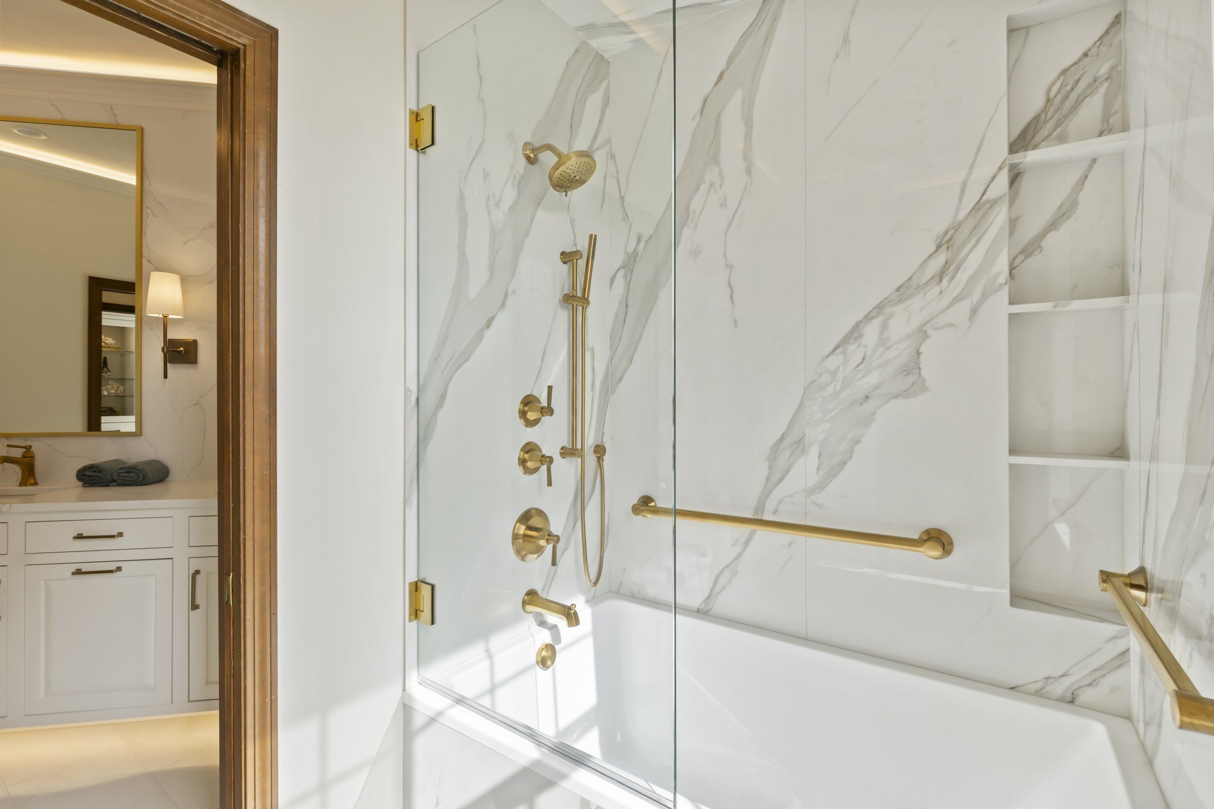 Tub and shower combination behind a frameless glass door, with brushed gold fixtures and grab bars