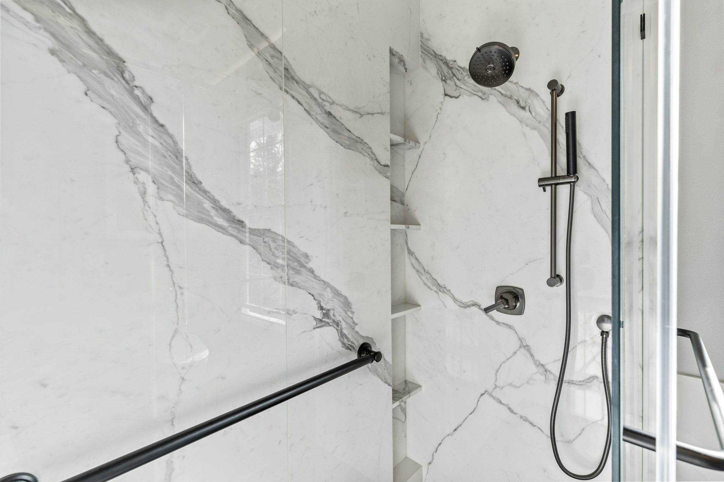 Matte black shower fixtures and handheld shower on marble-look panels