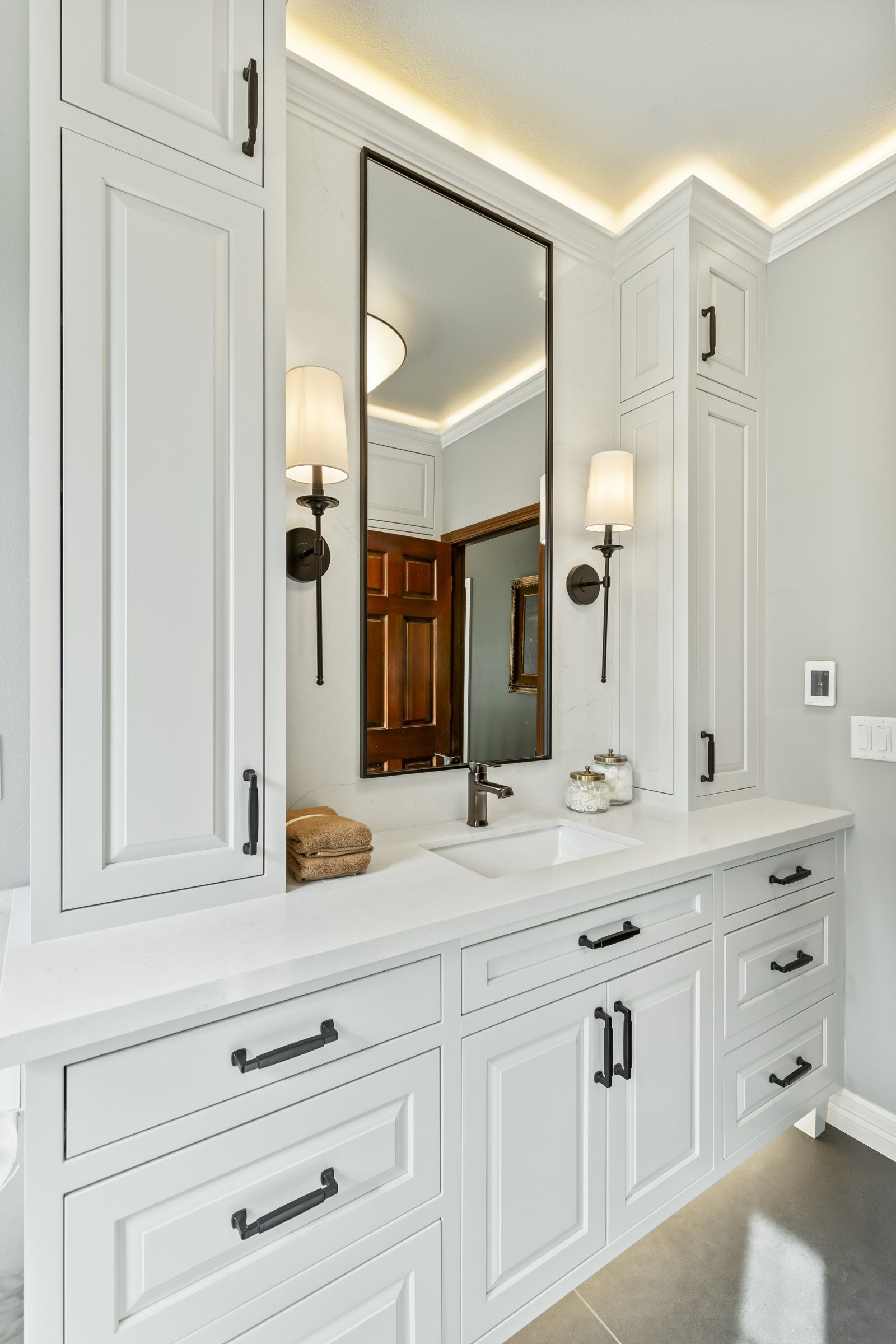 Vanity with a black-framed mirror, sconces and a tall storage cabinet
