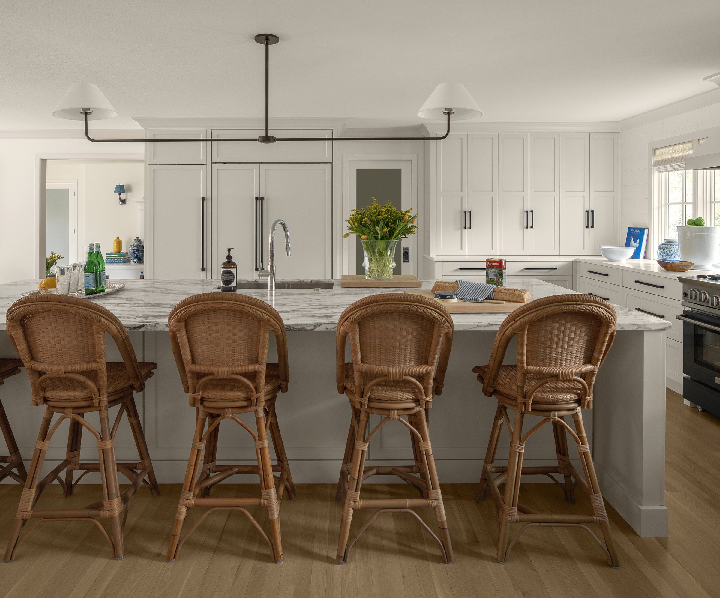 Remodeled white kitchen with a long marble island, rattan counter stools and a black pendant light