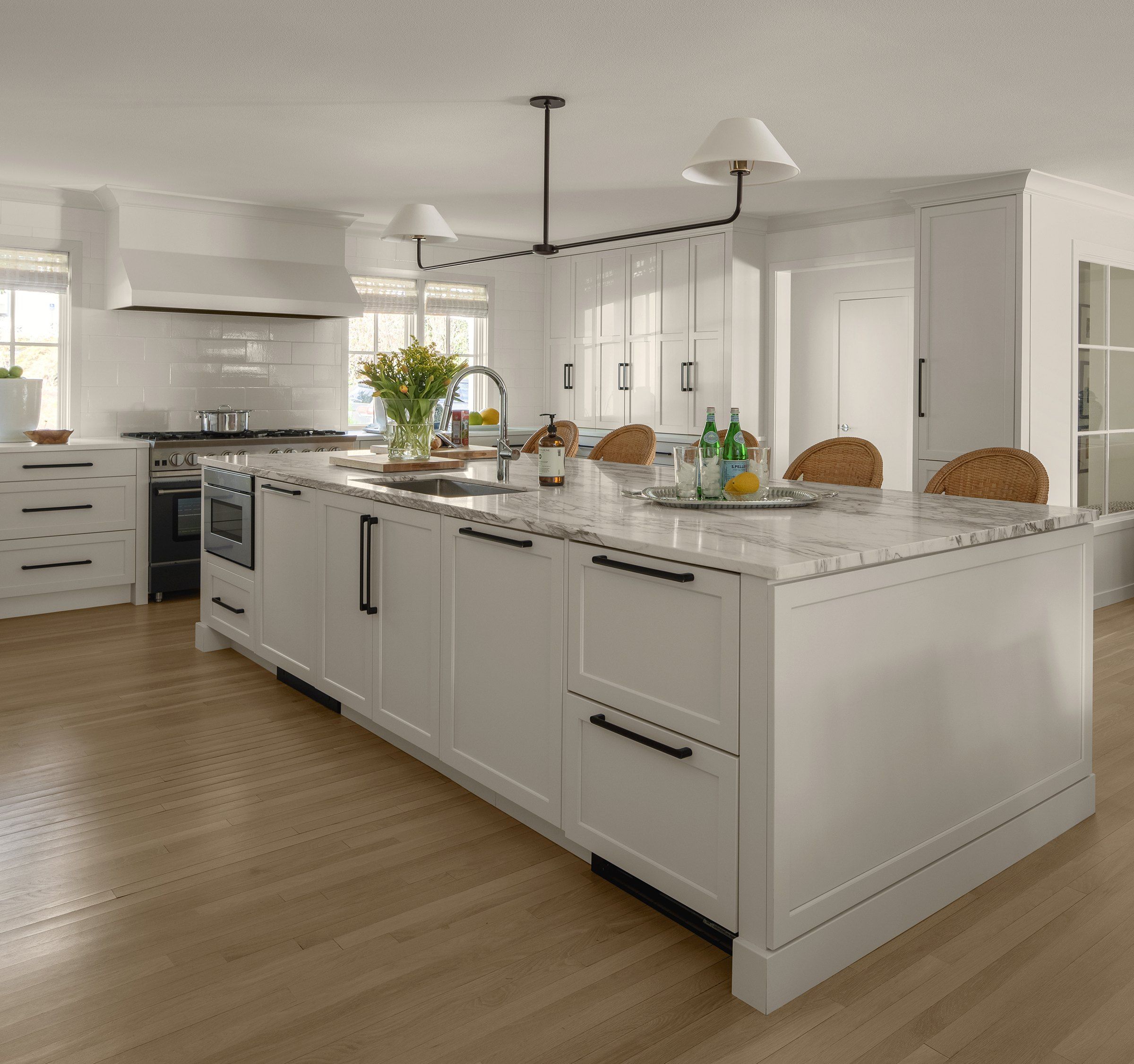 Wide view of the white kitchen with a marble island; behind the island at right, a shallow cabinet matched to the wall cabinets conceals the structural post