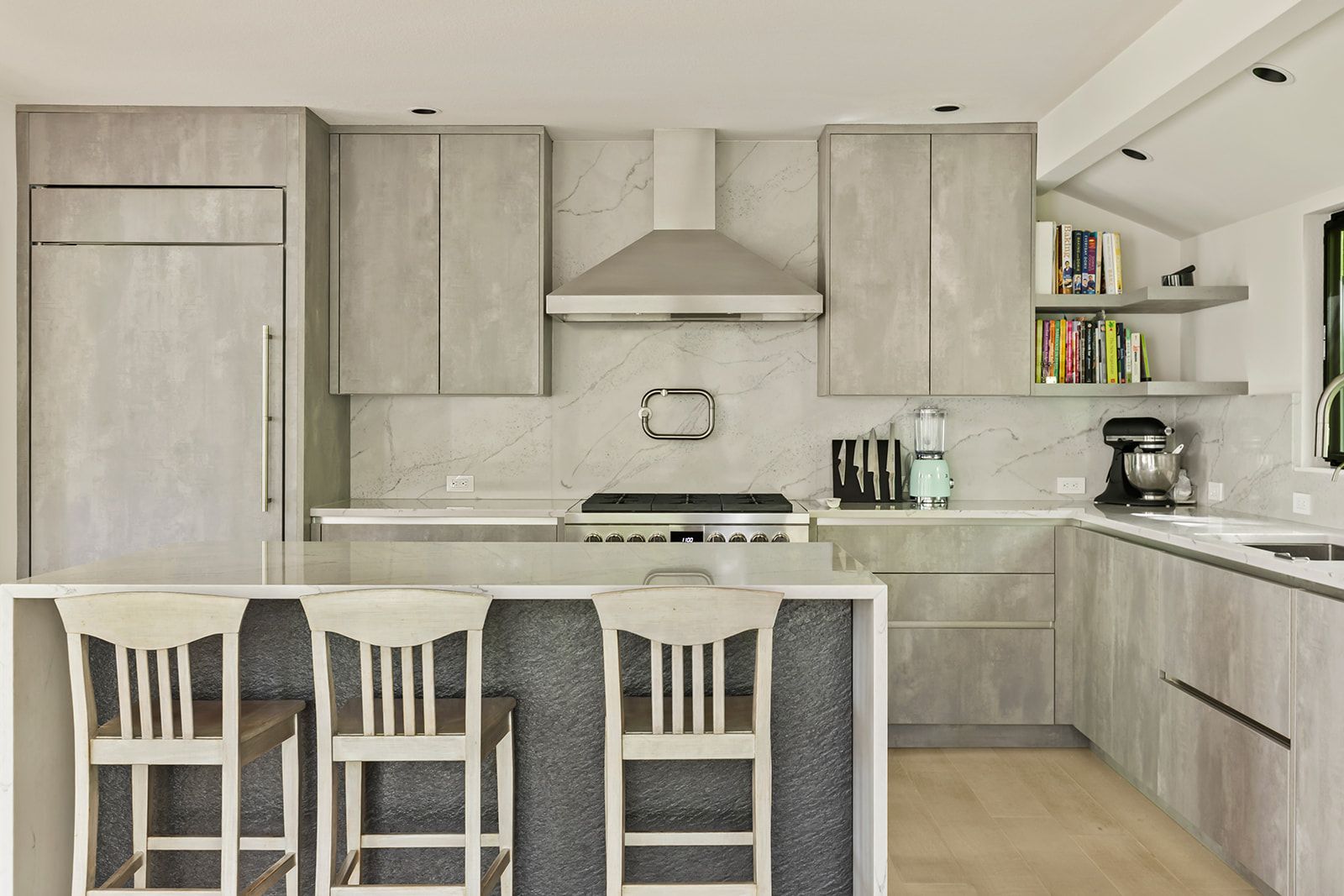 Modern kitchen with gray slab cabinets, a waterfall quartz island with seating, and a stainless range under a chimney hood