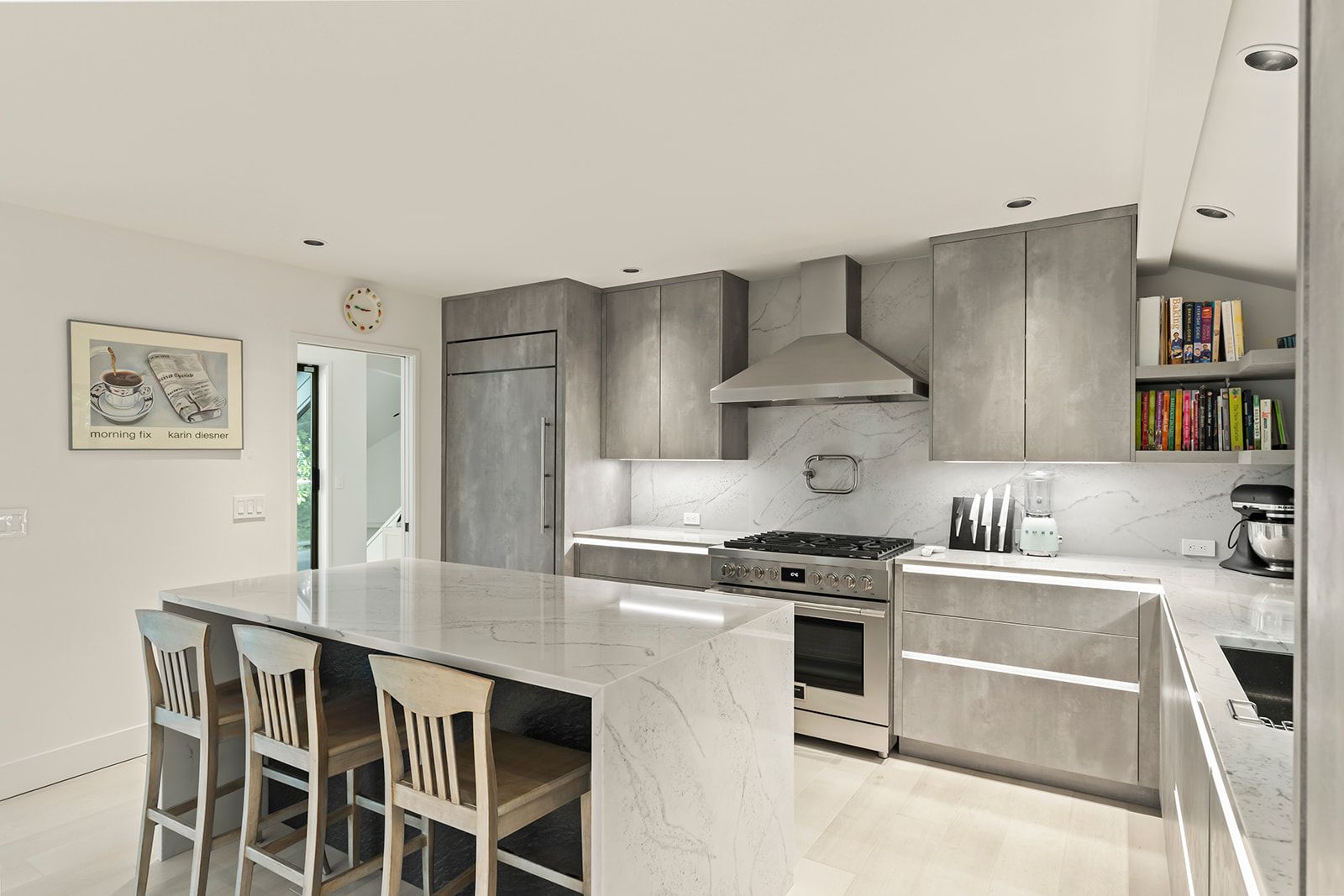 Remodeled kitchen with gray flat-panel cabinets, marble-look quartz backsplash and an island with three counter stools