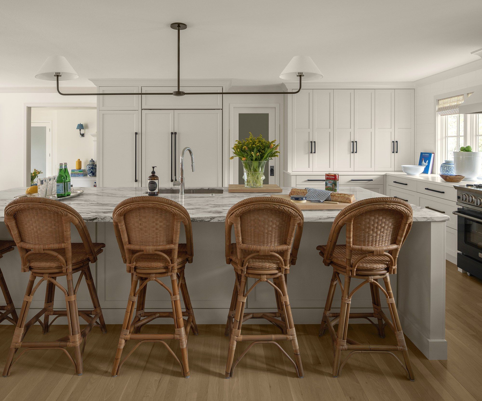 White kitchen with a long marble-topped island, rattan counter stools and a black pendant light