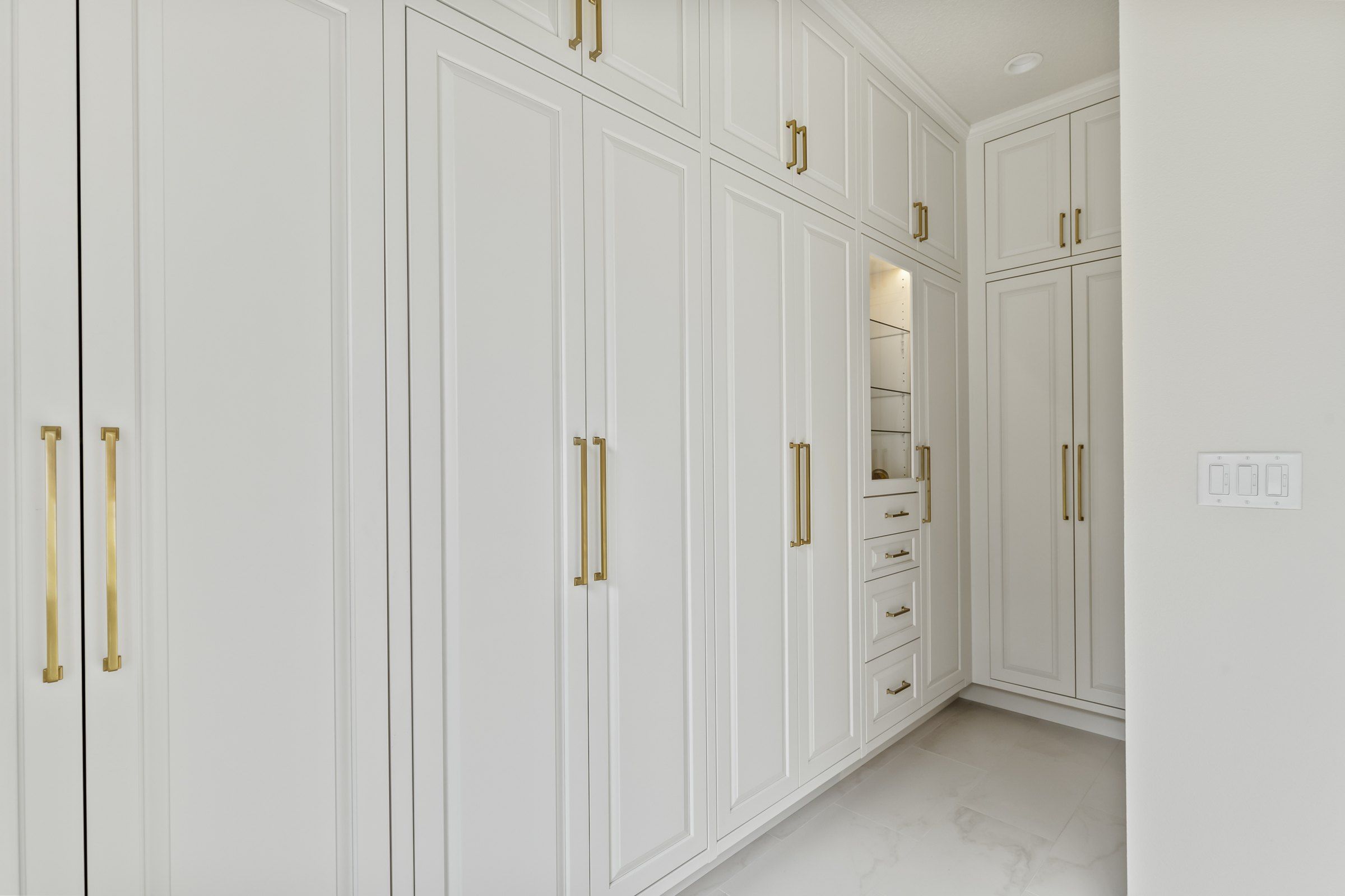 Wall of tall white linen cabinets with brass pulls