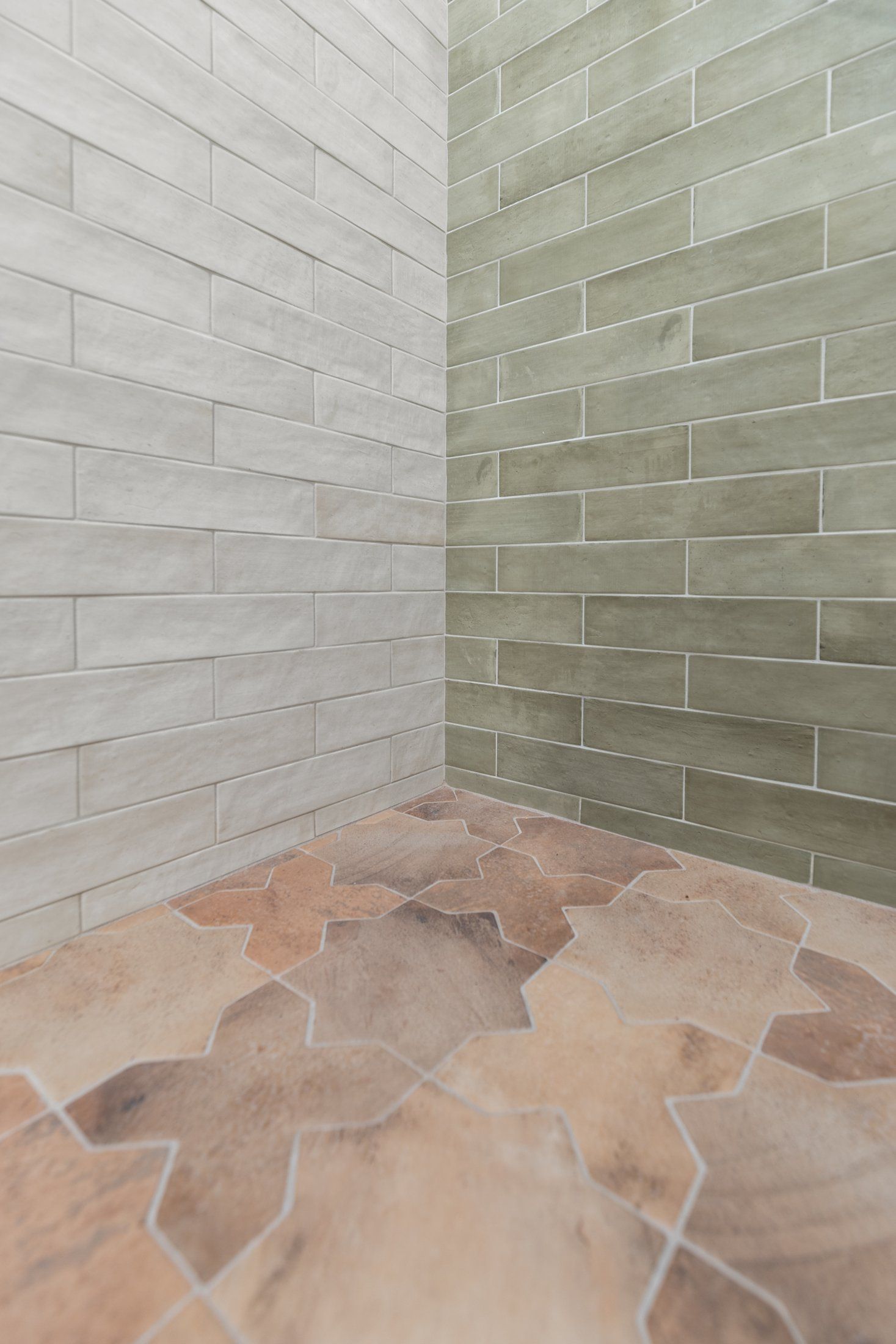 Terracotta-toned shower floor tile meeting green and white wall tile