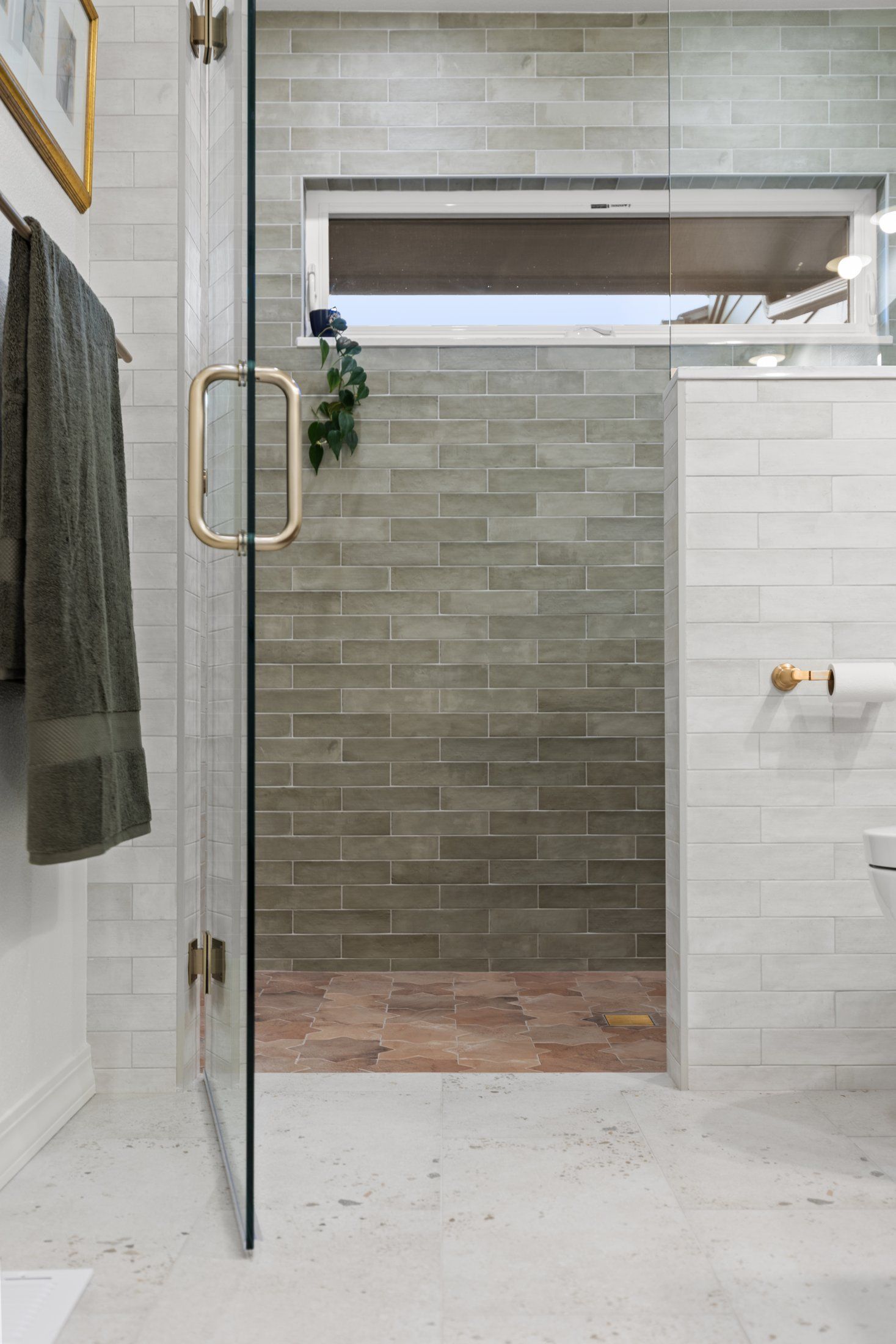 Frameless glass shower door with brass handle beside a white tile pony wall