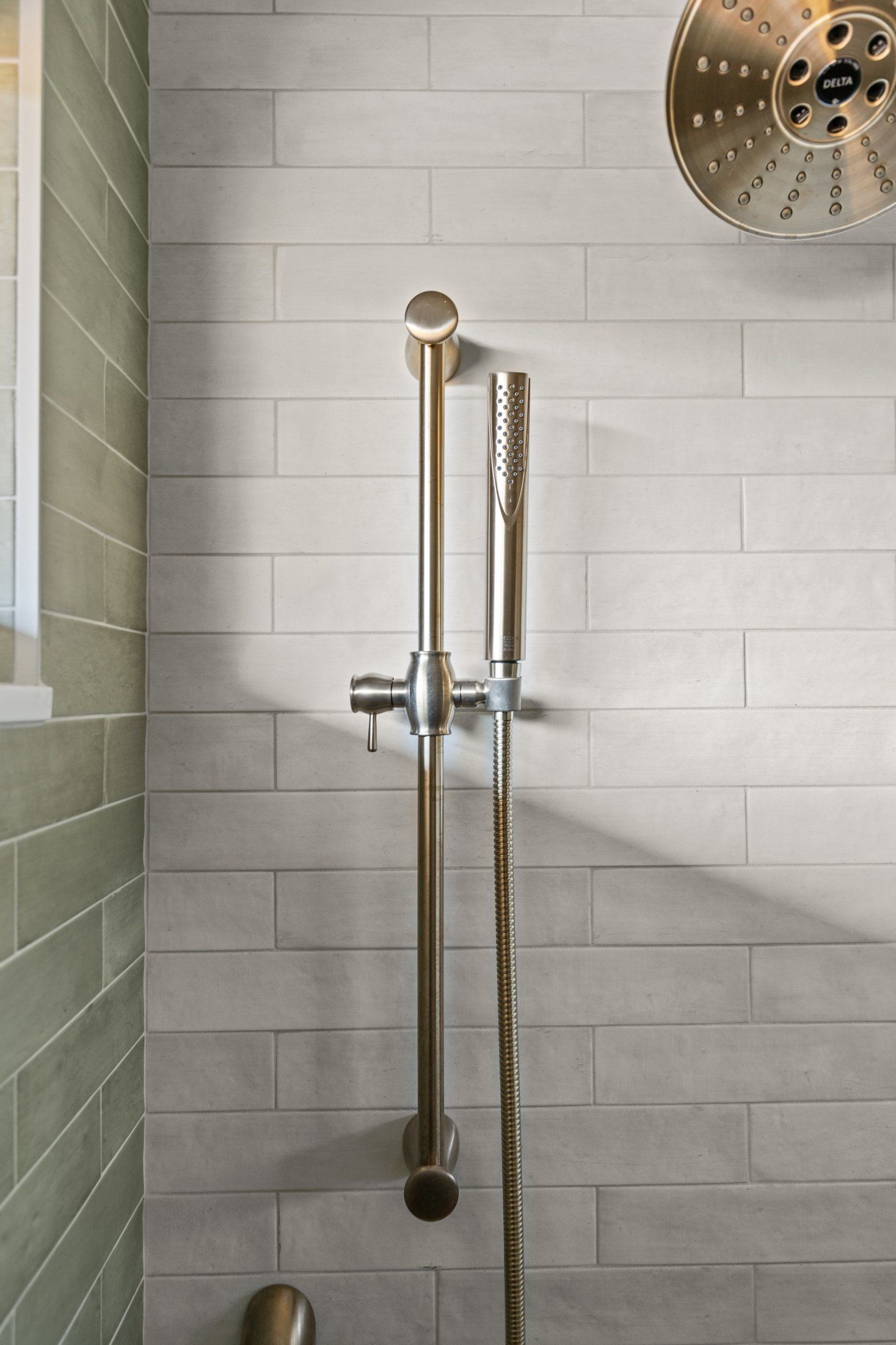 Brushed brass handheld shower on a slide bar against white and green tile