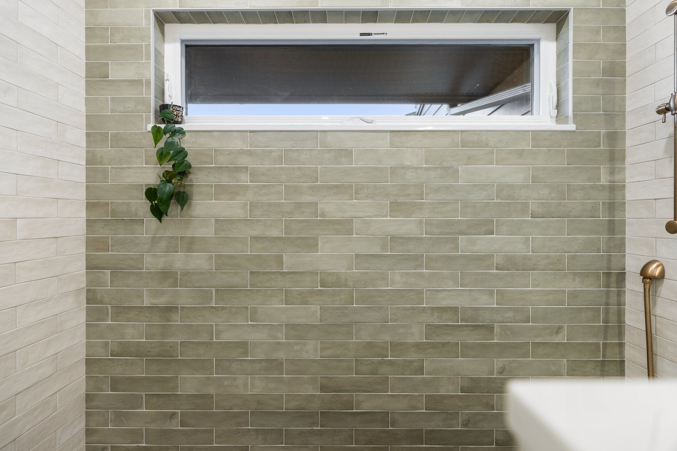 Green subway tile shower wall with a long horizontal hopper window above