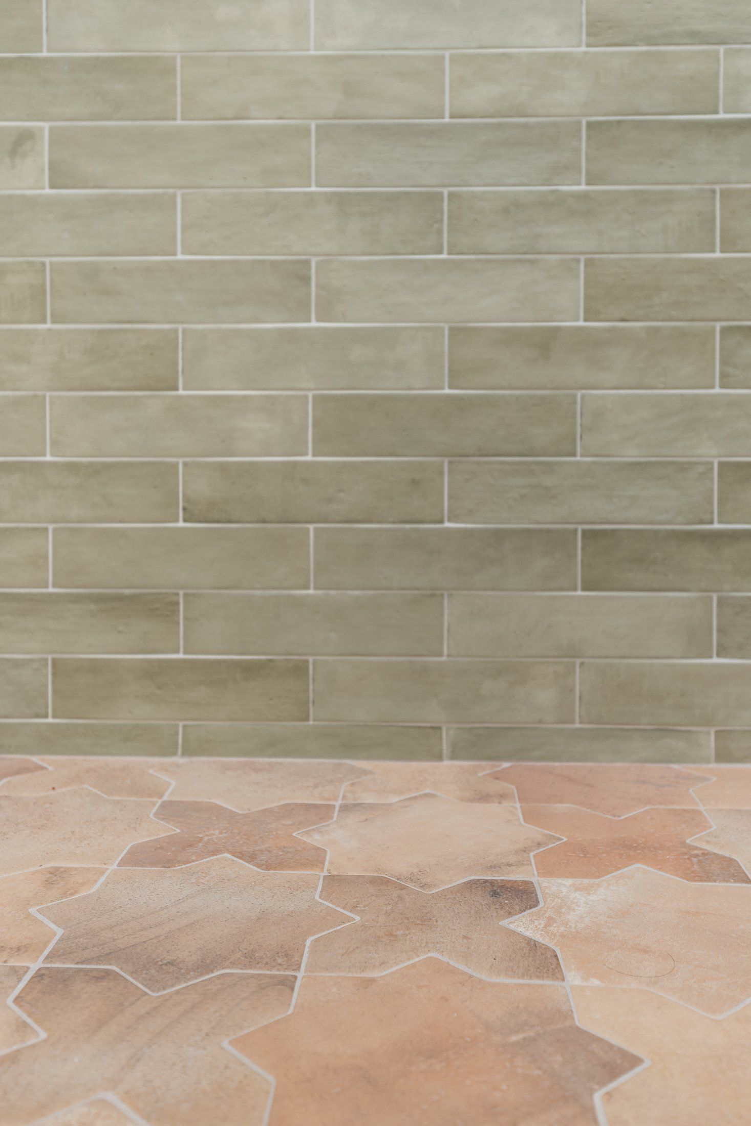 Green subway tile meeting a terracotta-colored shower floor